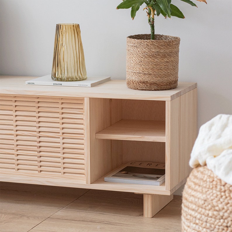 Puede incluir: Un armario de madera clara con dos puertas y un estante. El armario tiene un dise&ntilde;o de listones en las puertas delanteras. El armario est&aacute; sobre un suelo de madera. Hay una planta en una cesta tejida encima del armario.