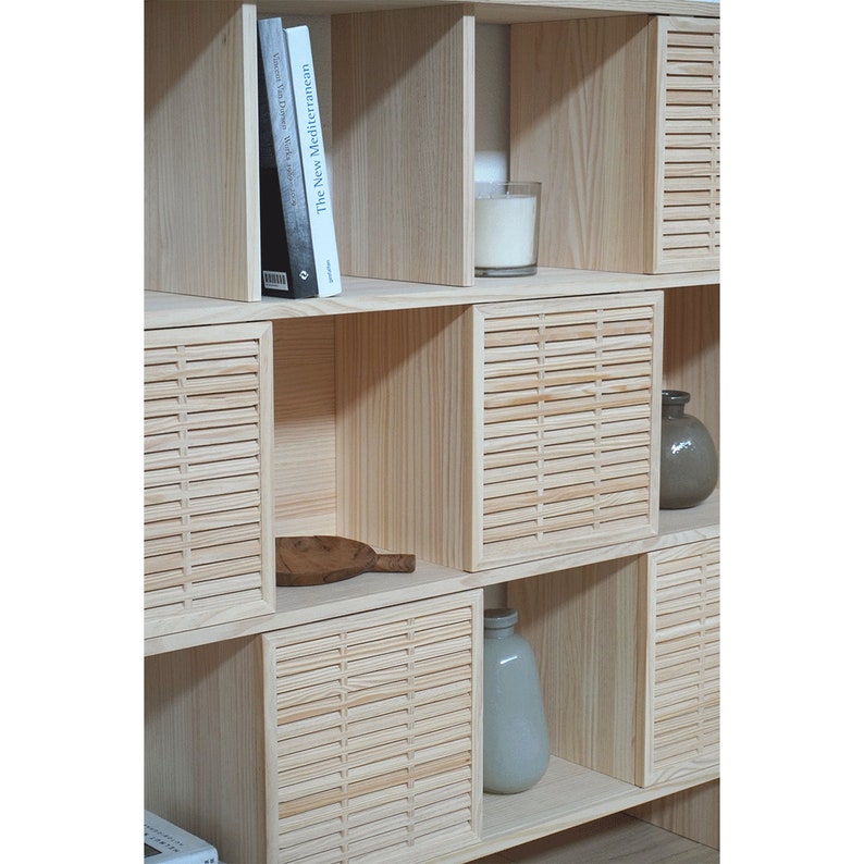 May include: A wooden bookshelf with slatted doors and shelves. The shelves are filled with books, vases, and candles. The bookshelf is made of light wood and has a natural finish.