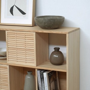 Op de afbeelding: Een houten plank met open vakken, met een grijze keramische kom, twee grijze keramische vazen en drie boeken met de titels "The New Mediterranean", "Vincent Van Duysen, Works" en "Vincent Van Duysen, How we work".