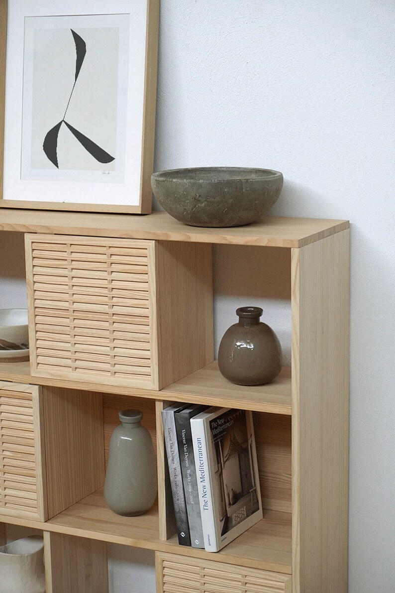 Op de afbeelding: Een houten plank met open vakken, met een grijze keramische kom, twee grijze keramische vazen en drie boeken met de titels "The New Mediterranean", "Vincent Van Duysen, Works" en "Vincent Van Duysen, How we work".
