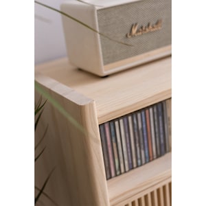 May include: A light wood CD storage cabinet with a shelf on top. The cabinet has a rounded edge and a speaker on top. The speaker is white with a gray grill and the text "Marshall" in gold.