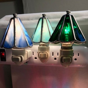 Picture of six lamp shade night lights plugged into outlets. They are blue, light blue, green, red, dark blue, and pink.