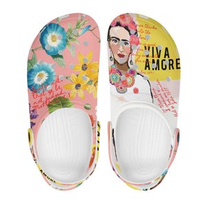 May include: A pair of white clogs with a floral and colorful design. One clog features a portrait of Frida Kahlo with the text "Viva Amore" and a bible verse. The other clog features a floral design with the text "Judge not, that ye be not judged."