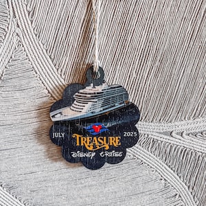 May include: A black, flower-shaped ornament with a cruise ship image and the text "TREASURE DISNEY CRUISE" with the dates "JULY 2025". The ornament is suspended by a natural twine string.
