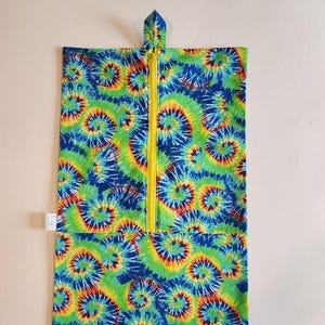 May include: A rectangular fabric pouch featuring a vibrant tie-dye pattern in shades of blue, green, yellow, and red. The pouch includes a vertical yellow zipper running down the center and a small fabric loop at the top for hanging purposes.