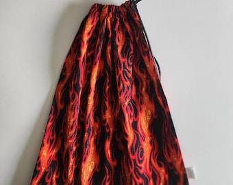 May include: A fabric drawstring pouch featuring a vibrant flame pattern in shades of red, orange, and yellow against a black background. The bag is gathered at the top with a thin black cord, creating a cinched closure for the storage container.