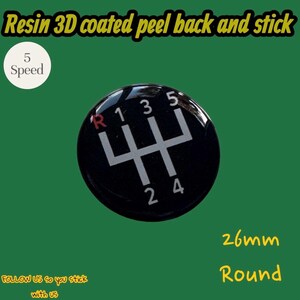 May include: A round, black, resin 3D coated peel back and stick emblem featuring a white 5-speed manual transmission gear shift pattern with a red R. The text 5 Speed and 26mm Round are visible, indicating the size of this automotive decal.