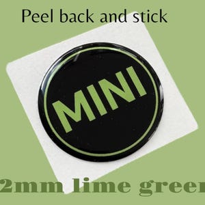 May include: A black and lime green round sticker with the word "MINI" in lime green letters. The sticker is 42 mm in diameter.