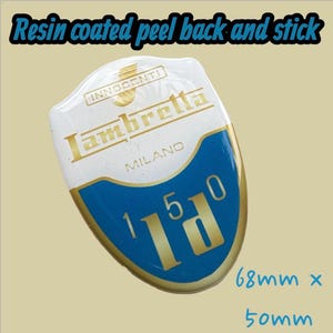 May include: A resin-coated, peel-and-stick Lambretta badge. The badge is white with gold lettering and a blue accent. It features the text "Lambretta MILANO" and "150". Dimensions are 68mm x 50mm.