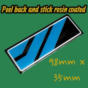 May include: A rectangular sticker with a resin coating, featuring a design of blue and black diagonal stripes. The sticker measures 98mm x 35mm, with the text "Peel back and stick resin coated" in yellow.