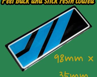 May include: A rectangular sticker with a resin coating, featuring a design of blue and black diagonal stripes. The sticker measures 98mm x 35mm, with the text "Peel back and stick resin coated" in yellow.