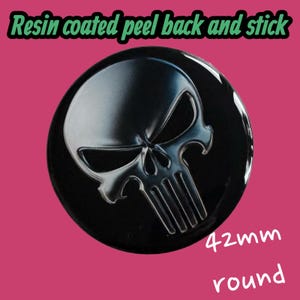 May include: A round, black resin-coated sticker with a peel-back adhesive. The sticker features a silver skull design. The text "Resin coated peel back and stick" is at the top, and "42mm round" is at the bottom.
