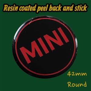 May include: A round, black sticker with the word "MINI" in red, resin-coated, peel-back design. The sticker has a red border and is 42mm in diameter. The text "Resin coated peel back and stick" is at the top.