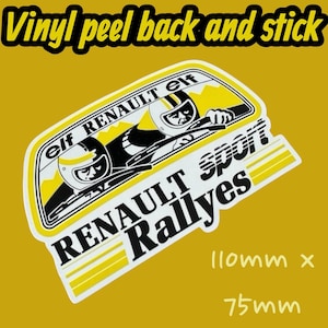 Op de afbeelding: Een vinyl sticker om te pellen en te plakken met de tekst "RENAULT Sport Rallyes" en de afbeelding van twee racers met helmen. De sticker is wit, zwart en geel en meet 110 mm x 75 mm.