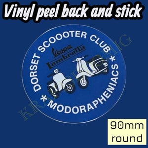 May include: A round blue sticker with white text and graphics. The text reads "DORSET SCOOOTER CLUB * MODORAPHENIACS" around the edge. Two white Vespa scooters are in the center. The sticker is 90mm round.