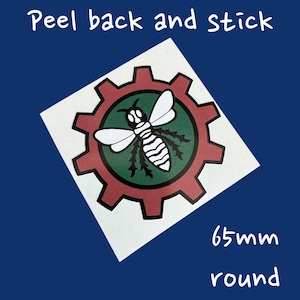 May include: A white sticker with a red and green gear design. The gear has a white bee with black stripes inside. The sticker is 65mm round and says "Peel back and stick".