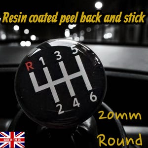 Può includere: Pomello del cambio rotondo in bianco e nero con schema a 6 marce. Il pomello ha numeri bianchi e una "R" rossa per la retromarcia. Il testo "Resin coated peel back and stick" è in alto. Il pomello è rotondo da 20 mm.