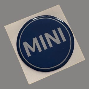 May include: A round, blue, 3D resin sticker with a silver "MINI" logo.