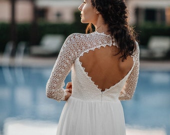 May include: A white lace wedding dress with a low back and long sleeves. The dress has a heart-shaped cutout in the back. The bride is standing in front of a swimming pool.