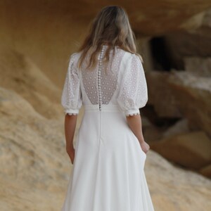 Puede incluir: Un vestido de novia blanco con un corpiño de encaje y una falda fluida. El vestido tiene una espalda con botones y una cola larga.