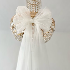May include: A white tulle bow tied around a gold crystal chandelier.