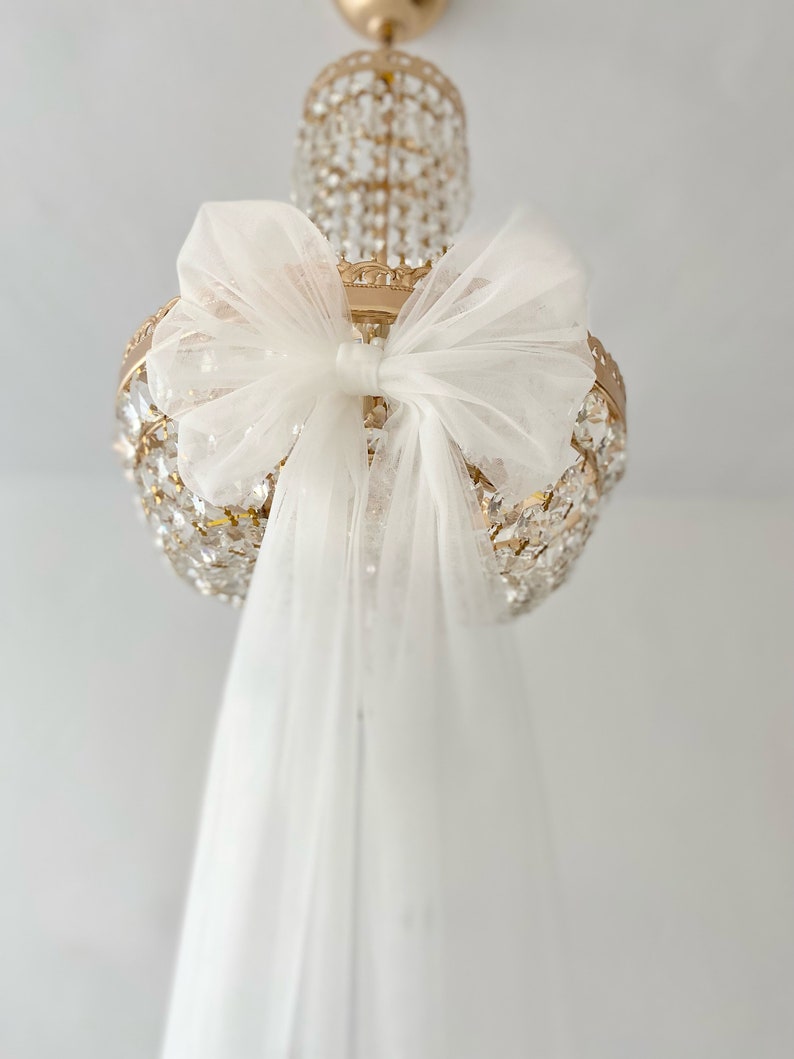 May include: A white tulle bow tied around a gold crystal chandelier.