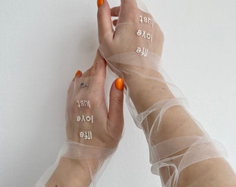 Könnte beinhalten: Ein Paar weiße, durchsichtige Handschuhe mit den Worten "life", "love" und "just", die auf der Rückseite jeder Hand gestickt sind.