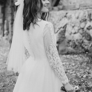 May include: A bride in a white lace wedding dress with a veil and a bouquet of white flowers.