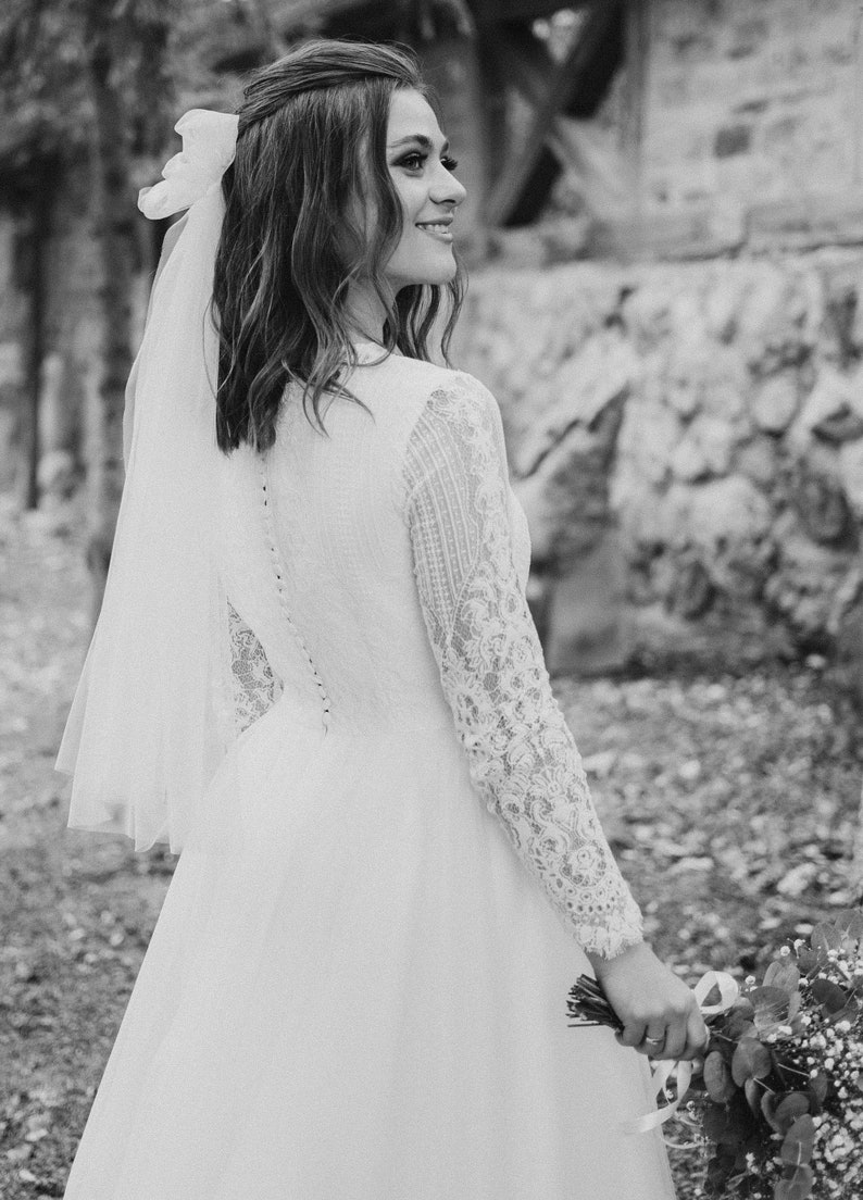 May include: A bride in a white lace wedding dress with a veil and a bouquet of white flowers.