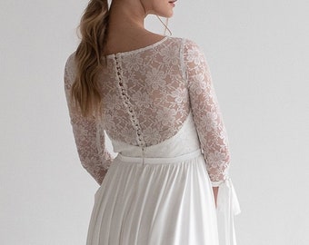 Könnte beinhalten: Ein weißes Brautkleid mit einem Spitzenoberteil und einem fließenden Rock. Das Oberteil hat einen runden Ausschnitt und lange Ärmel mit Knopfdetails. Der Rock ist aus einem glatten, fließenden Stoff.