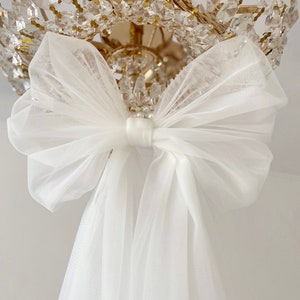 May include: A white tulle bow tied around a crystal chandelier.