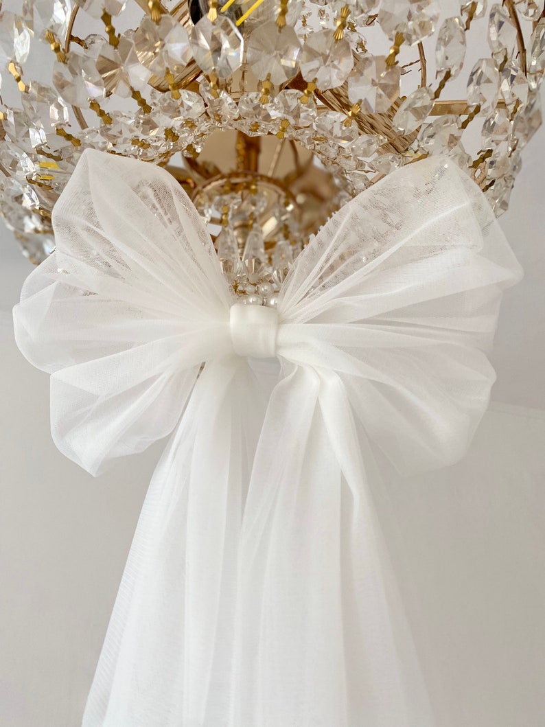 May include: A white tulle bow tied around a crystal chandelier.