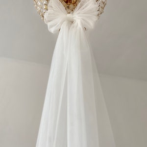 May include: A white tulle bow tied around a gold chandelier. The tulle drapes down from the bow.
