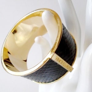 May include: A wide gold and black bangle bracelet with the text "Vince Camuto" engraved on the black portion.