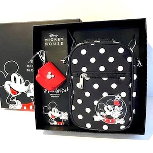 May include: A black gift set featuring Disney's Mickey Mouse. The set includes a crossbody bag with white polka dots, a red coin purse, and a small pouch. The bag has a Mickey Mouse graphic on the front. The gift set is in a black box with Mickey Mouse graphics.