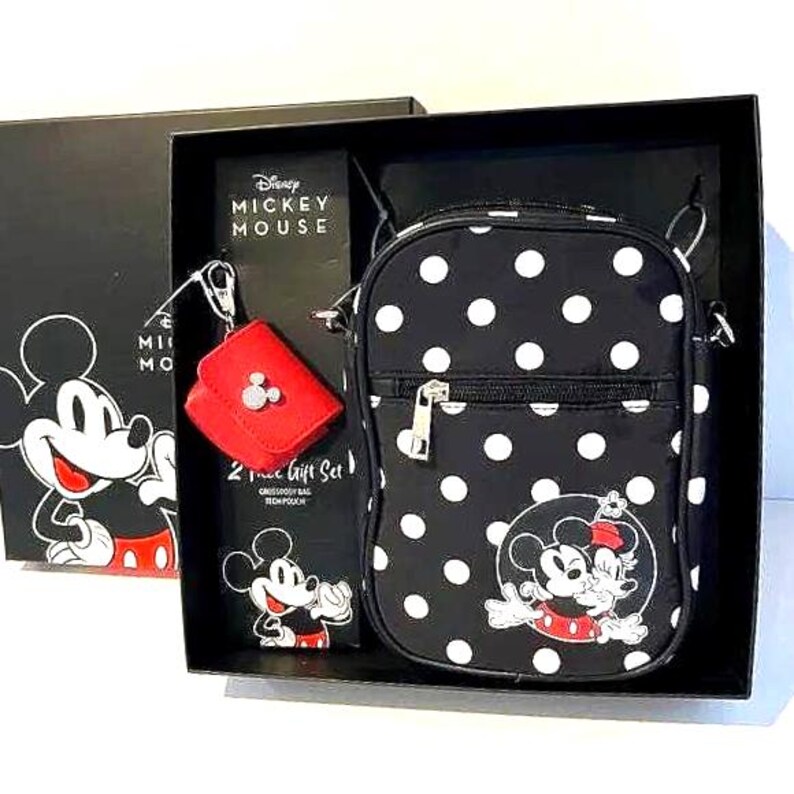 May include: A black gift set featuring Disney's Mickey Mouse. The set includes a crossbody bag with white polka dots, a red coin purse, and a small pouch. The bag has a Mickey Mouse graphic on the front. The gift set is in a black box with Mickey Mouse graphics.