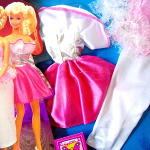 Puede incluir: Dos muñecas Barbie con vestidos rosa y blanco. Las muñecas tienen el pelo rubio y llevan joyas de plata. Las muñecas forman parte de un conjunto que incluye un vestido blanco con ribetes rosas y una falda blanca con ribetes rosas.