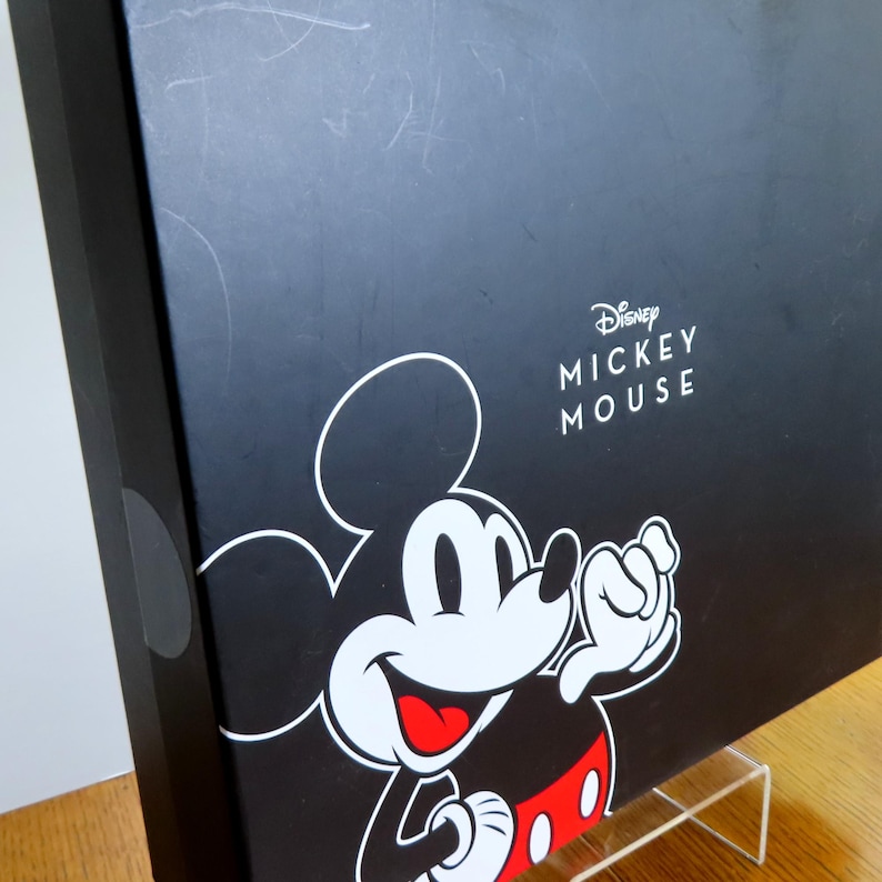 May include: Black box featuring a large Mickey Mouse graphic in white, red, and black. The Disney Mickey Mouse logo is printed in white. The box is displayed on a clear acrylic stand.