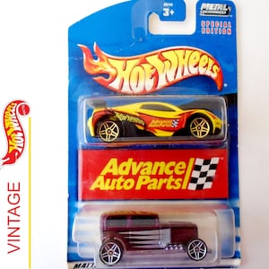 May include: A Hot Wheels die-cast car set featuring a purple and silver 1932 Ford Coupe and a yellow and black Advance Auto Parts race car. The cars are packaged in a blue and red cardboard box with the Hot Wheels logo and the words "Metal Special Edition".
