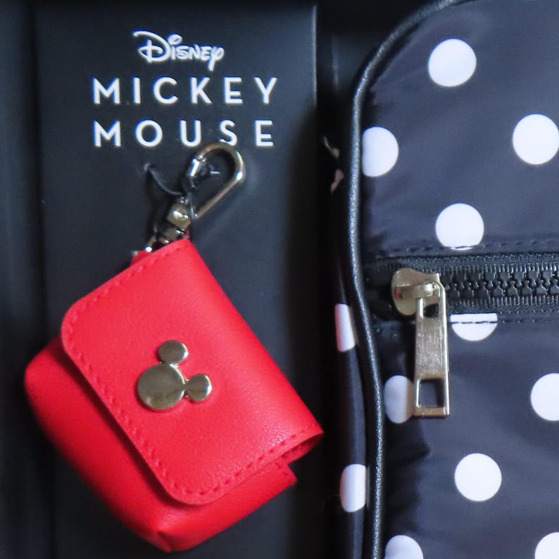 May include: A red leatherette case with a silver Mickey Mouse emblem, attached to a black box with "Disney Mickey Mouse" text. A black and white polka dot bag is visible in the background.