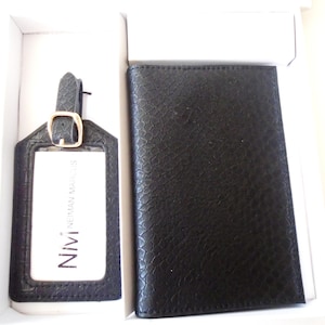 May include: Black leather travel set with a luggage tag and passport holder. The luggage tag has a clear window for a name tag and the text "NIVI" and "ONE MAN MARKS" printed on it.