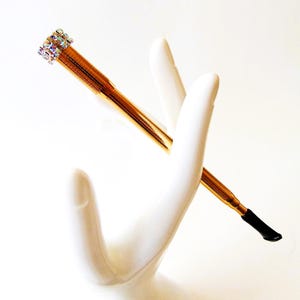 May include: A gold-colored cigarette holder with a black tip and a clear rhinestone embellishment at the top.