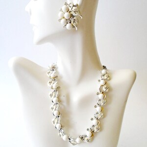 Op de afbeelding: Een witte en zilveren ketting en oorbellen set met grote witte kralen. De ketting is een ketting met een gekoppeld ontwerp en de oorbellen zijn een cluster van witte kralen.