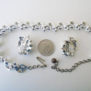 Op de afbeelding: Een zilverkleurige ketting en oorbellen set met nepparels en strass. De ketting heeft een kettingverlenger en de oorbellen hebben clip-sluitingen.