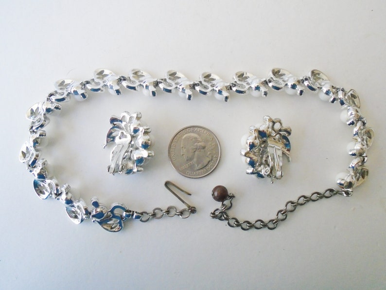 Op de afbeelding: Een zilverkleurige ketting en oorbellen set met nepparels en strass. De ketting heeft een kettingverlenger en de oorbellen hebben clip-sluitingen.