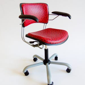 May include: A red and black office chair with a patterned seat and backrest. The chair has black armrests, a black and grey base, and small wheels. The chair is designed for comfort and support.