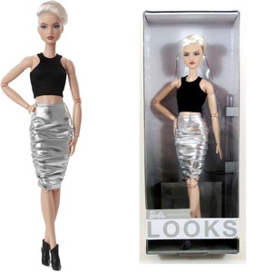 May include: A Barbie Signature doll with short blonde hair wearing a black crop top and a silver skirt. The doll is in a box with the words "Barbie Signature Looks" on the front.