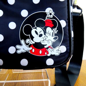 May include: Black shoulder bag with white polka dots and a graphic of Mickey and Minnie Mouse kissing. The bag has a black strap and a white outline of the characters. The bag is made of a durable material.