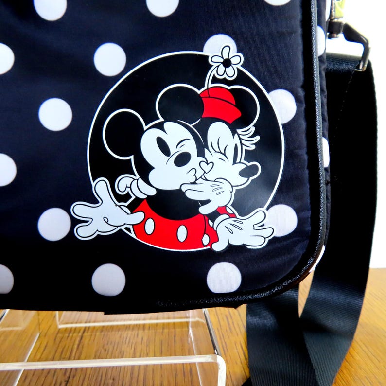 May include: Black shoulder bag with white polka dots and a graphic of Mickey and Minnie Mouse kissing. The bag has a black strap and a white outline of the characters. The bag is made of a durable material.