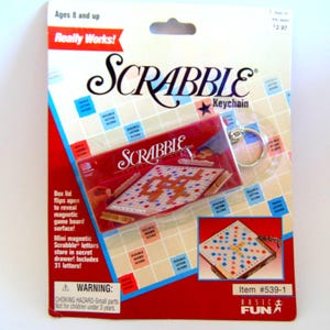 May include: A Scrabble keychain on a red and white package. The keychain features a miniature Scrabble game board and includes 31 magnetic letters. The package has the text "Really Works!" and "Ages 8 and up."